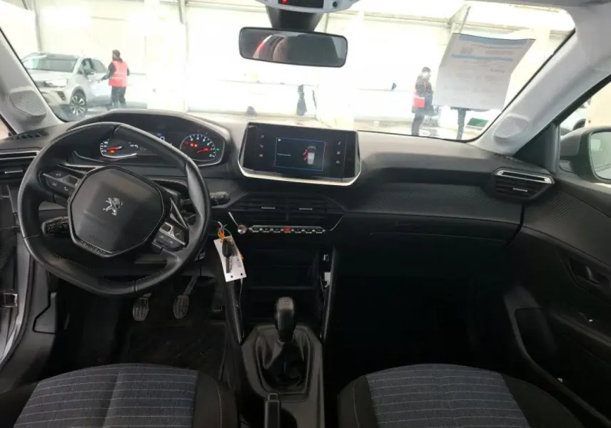 Vue intérieure avant de la Peugeot 208 1.2i 12V avec tableau de bord noir et volant compact au centre.