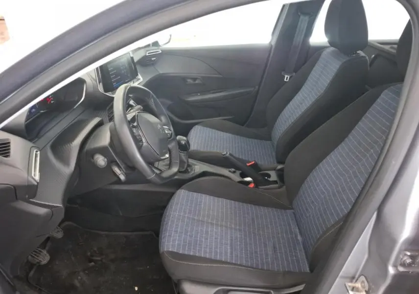 Vue intérieure côté conducteur de la Peugeot 208 gris Artense, montrant les sièges tissu bleu et la planche de bord noire.