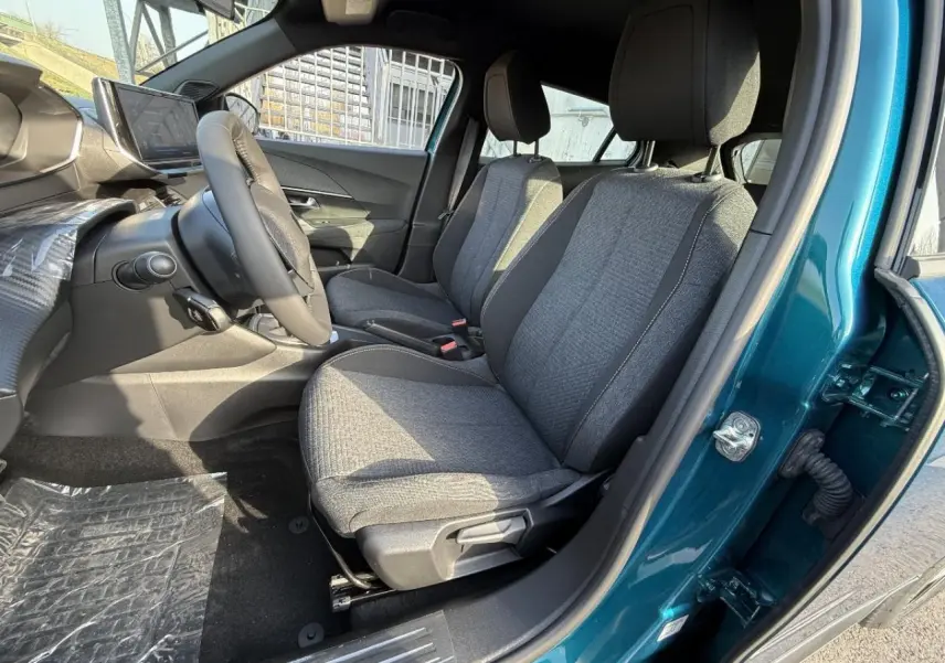 Vue intérieure côté conducteur du Peugeot 2008 2025 bleu obsession, montrant les sièges avant en tissu gris et le volant.