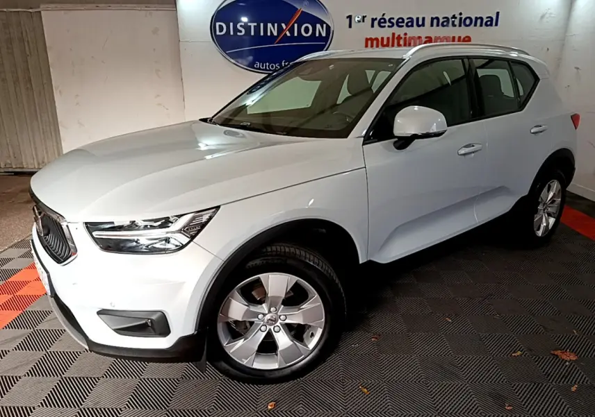 Vue 3/4 avant d'un Volvo XC40 gris clair garé en intérieur avec jantes alliage et calandre noire distinctive.