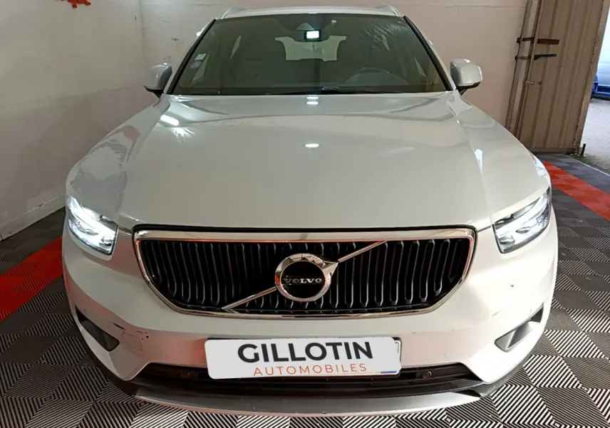 Vue frontale d'un Volvo XC40 gris clair avec calandre noire et phares LED allumés dans un garage.