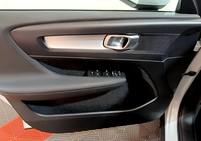 Gros plan sur la porte avant gauche intérieure du Volvo XC40 gris clair, avec poignée argentée et commandes électriques.