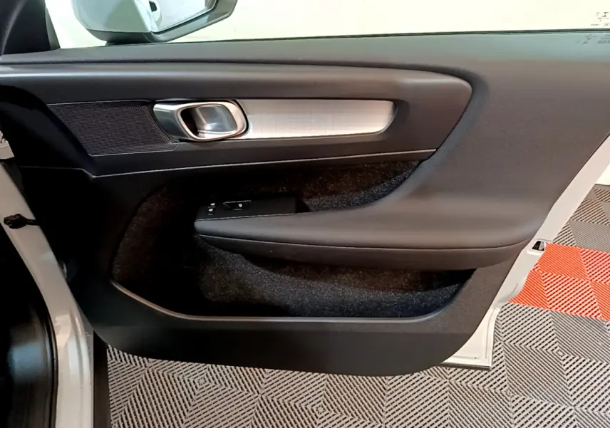 Intérieur montrant la porte côté gauche du Volvo XC40 gris clair avec poignée argentée et commandes de vitres.