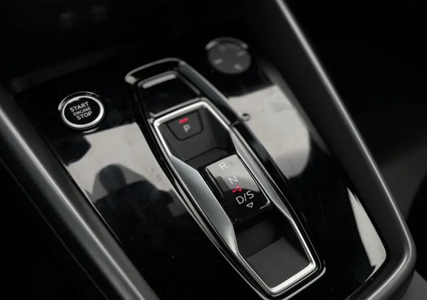 Gros plan sur la console centrale noire brillante avec levier de vitesses automatique et bouton Start/Stop d'une Audi A3 Berline.