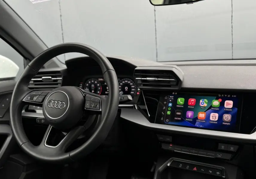 Vue intérieure de l'Audi A3 Berline 2024 côté conducteur, volant cuir et écran tactile multimédia allumé.