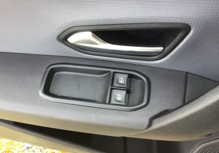 Gros plan sur la poignée intérieure et les commandes des vitres côté gauche d’un Renault Express Van blanc 2023.