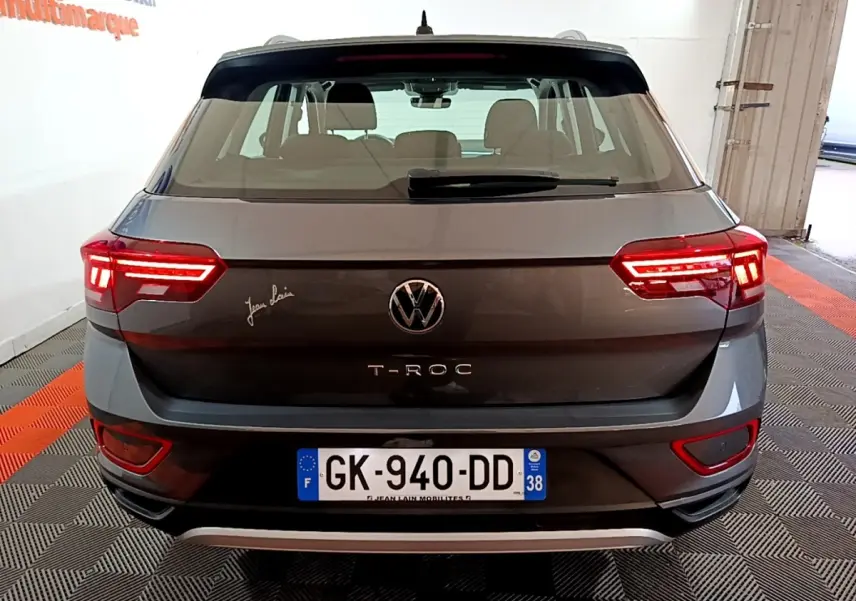 Vue arrière d’un Volkswagen T-Roc gris foncé avec feux allumés et plaque d’immatriculation française visible.