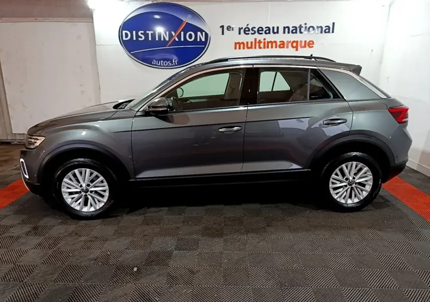 Vue de profil côté gauche d’un Volkswagen T-Roc gris foncé 2022, avec jantes alliage et barres de toit noires.