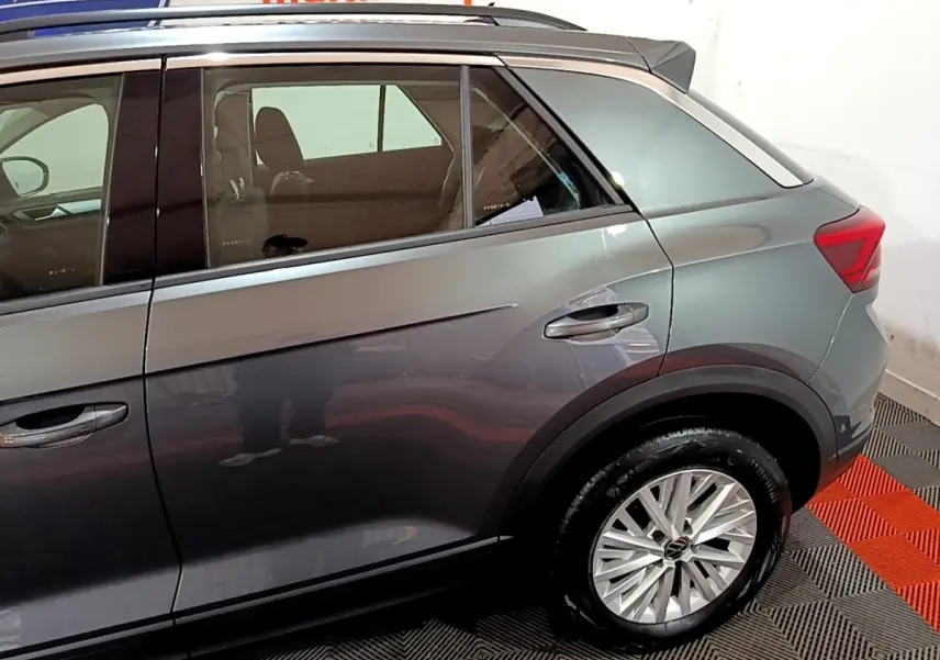 Vue latérale côté droit du Volkswagen T-Roc gris foncé, mettant en valeur la porte arrière et la roue arrière avec jante alliage.