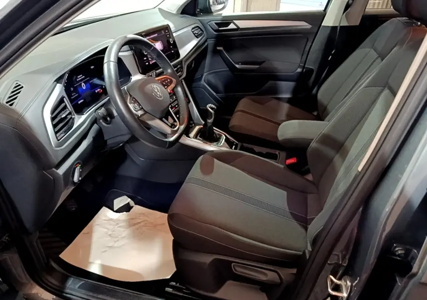 Vue intérieure côté conducteur du Volkswagen T-Roc gris foncé 2022, avec volant cuir et écran tactile central.