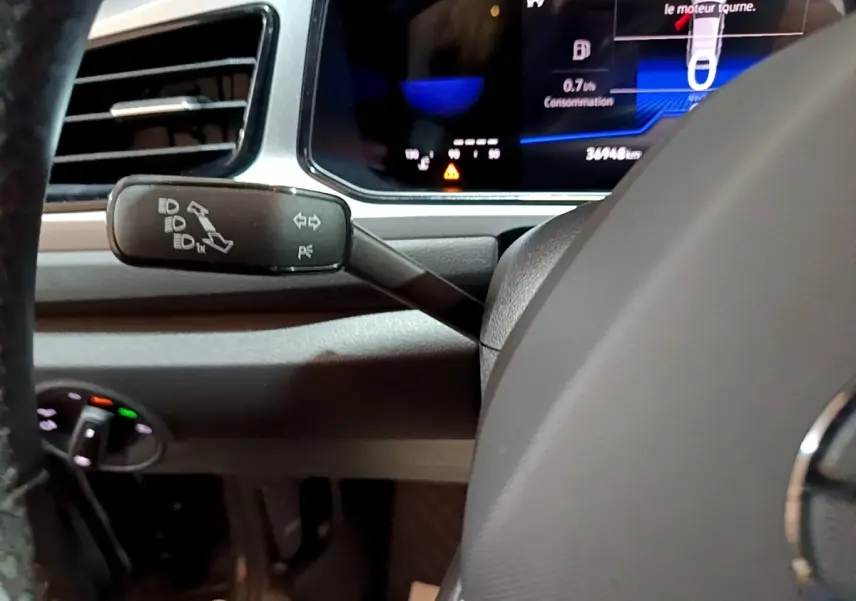 Gros plan sur la manette de clignotants à gauche du volant d’un Volkswagen T-Roc gris foncé, tableau de bord numérique visible.