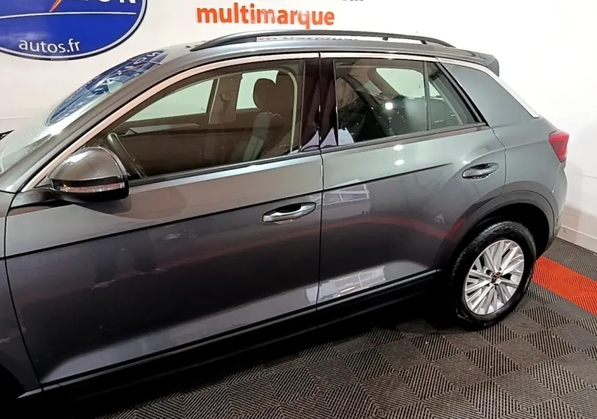 Vue latérale côté gauche du Volkswagen T-Roc gris foncé 2022, mettant en valeur les jantes et la ligne de toit chromée.