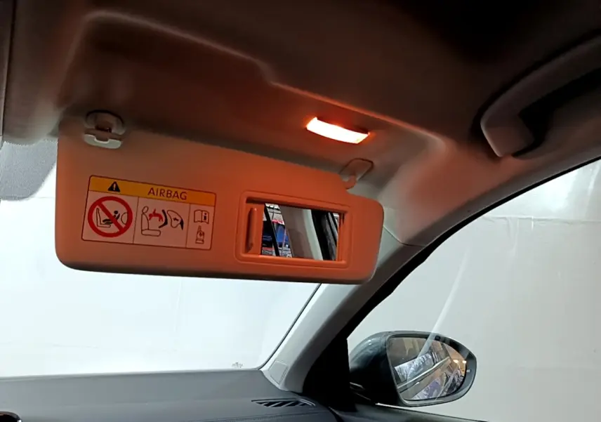 Vue intérieure côté passager du pare-soleil beige avec miroir et rétroviseur extérieur noir visible sur un Volkswagen T-Roc gris foncé.