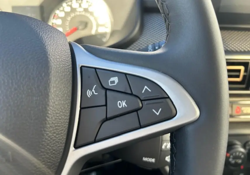 Gros plan sur les commandes au volant côté droit du Dacia Sandero Stepway blanc, avec boutons multifonctions et finition argentée.