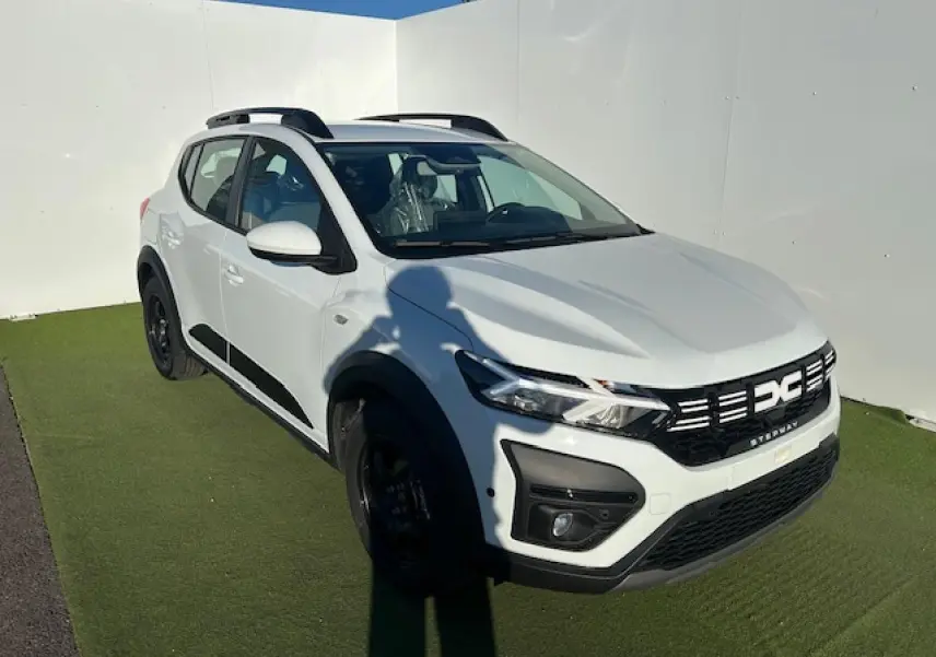 Dacia Sandero Stepway blanc arctique vue 3/4 avant droit avec barres de toit noires et signature lumineuse LED.