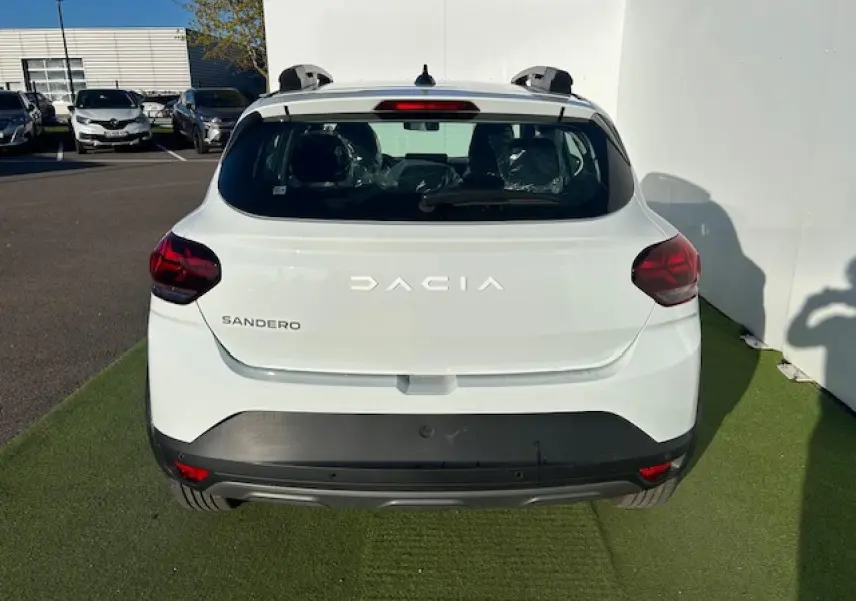 Vue arrière d'une Dacia Sandero blanche Arctic avec feux arrière en Y et barres de toit visibles.