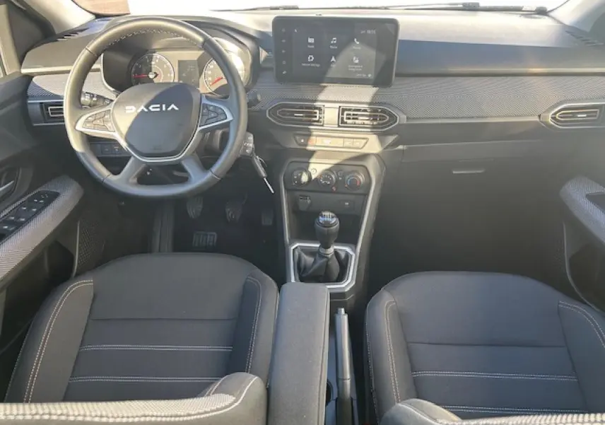 Vue intérieure avant centrée sur le tableau de bord et volant noir de la Dacia Sandero Stepway 2025 avec écran tactile 8 pouces.