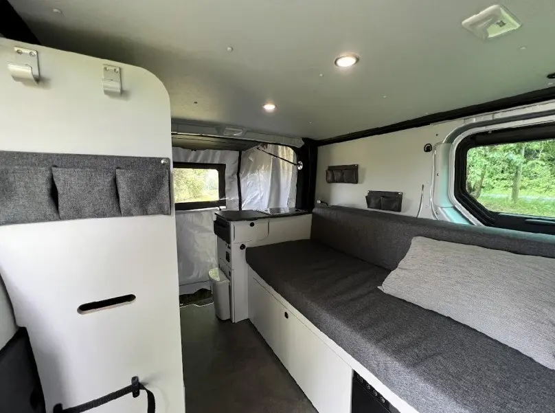 Intérieur du Renault Trafic Fourgon aménagé, vue latérale droite montrant banquette grise et rangements blancs.