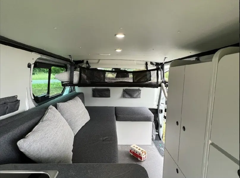 Intérieur du Renault Trafic Fourgon aménagé, vue latérale droite sur banquette grise et rangements blancs.