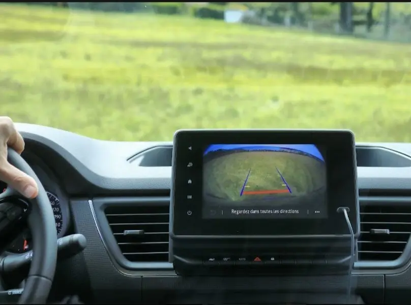 Vue intérieure centrée sur l'écran de la caméra de recul du Renault Trafic Fourgon gris, volant à gauche visible.