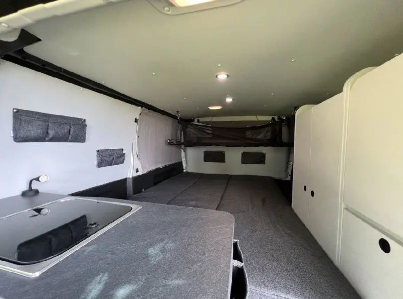 Intérieur aménagé du Renault Trafic Fourgon gris, vue de l'arrière vers l'avant avec espace couchage et rangements.