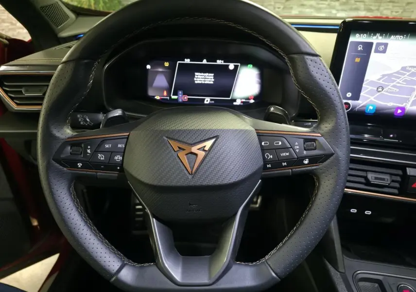 Vue rapprochée du volant en cuir perforé noir avec logo CUPRA cuivre et tableau de bord digital du Formentor rouge 2024.