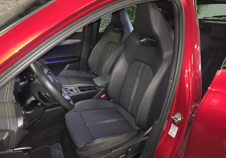 Vue intérieure côté conducteur du CUPRA Formentor 1.4 e-Hybrid 2024 rouge, sièges baquets noirs avec surpiqûres cuivre.