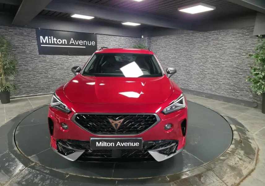 Vue avant d'une CUPRA Formentor rouge Désir 2024 avec calandre noire et logo cuivre, sur plateau tournant intérieur.