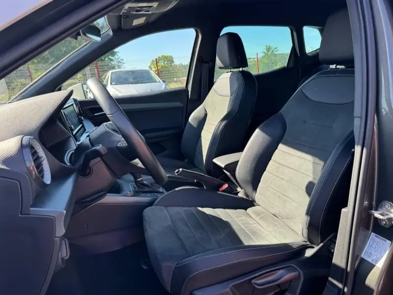 Vue intérieure côté conducteur du SEAT Arona noir 2025, sièges tissu gris Sano avec volant cuir multifonction.