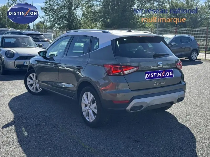 Vue 3/4 arrière droite d'un SEAT Arona gris avec toit blanc et jantes alu, stationné en extérieur au soleil.