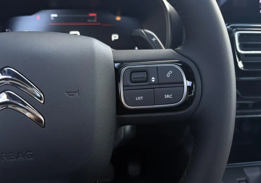 Gros plan sur le volant noir du Citroën C5 Aircross 2025, avec commandes intégrées à droite et palettes au volant visibles.