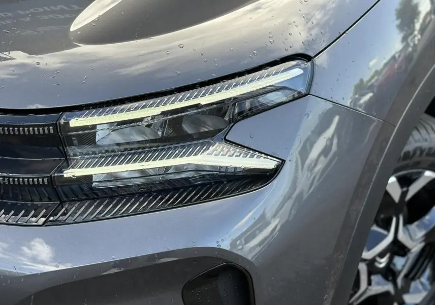 Gros plan sur le phare avant droit du Citroën C5 Aircross gris Platinium avec jante alliage visible en arrière-plan.