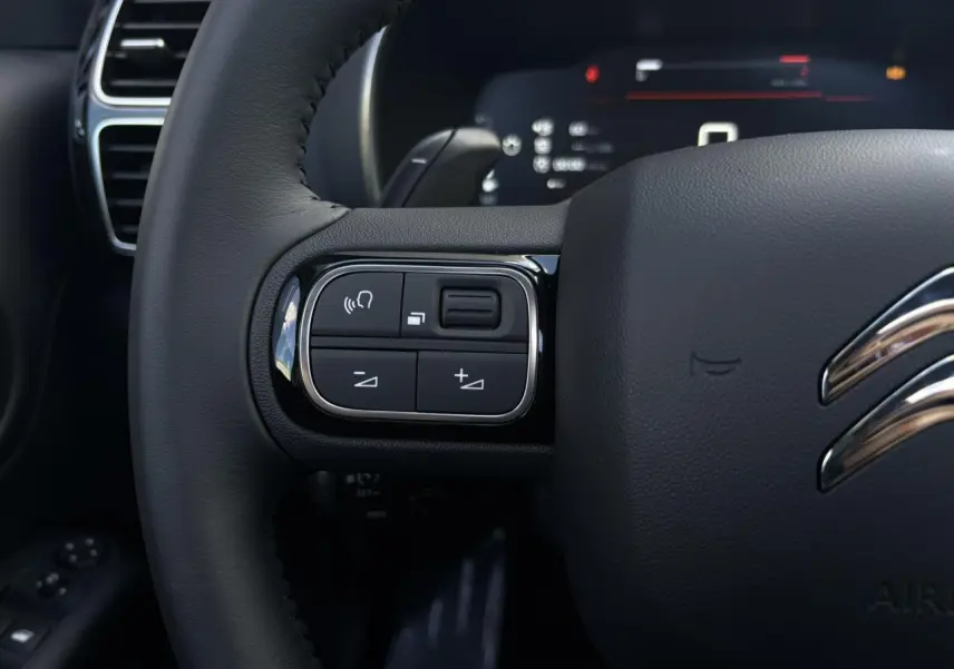 Gros plan sur les commandes gauche du volant cuir noir du Citroën C5 Aircross 2025, détails chromés et touches fonctionnelles.