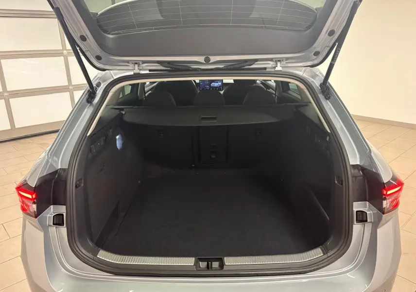 Coffre ouvert vu de l'arrière d'une Skoda Superb Combi gris argent 2025, intérieur spacieux et habillage noir.