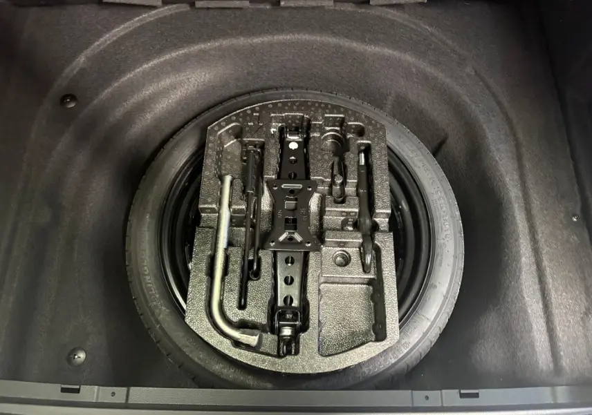 Vue plongeante sur la roue de secours et les outils de bord dans le coffre d'une Skoda Superb Combi gris argent 2025.