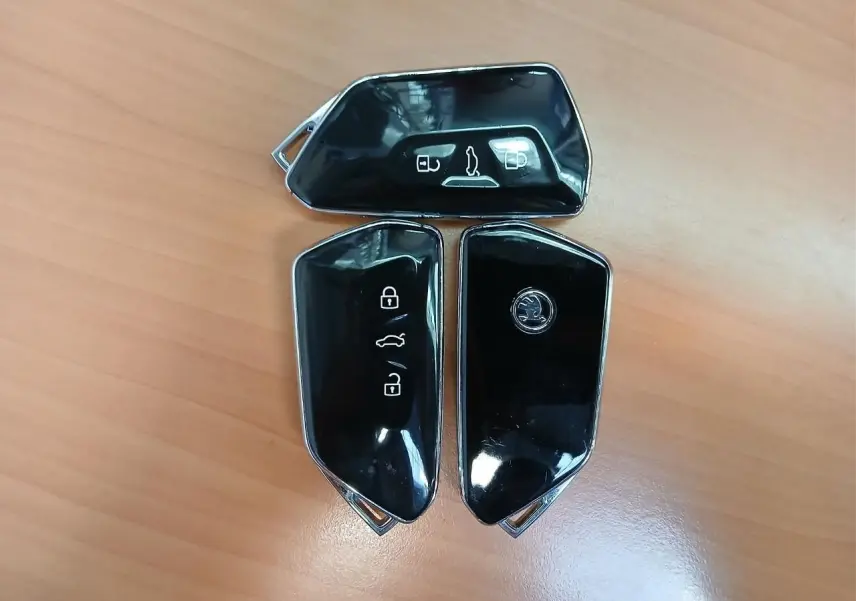Trois clés noires brillantes de SKODA Superb Combi 2025 posées sur un bureau en bois clair.
