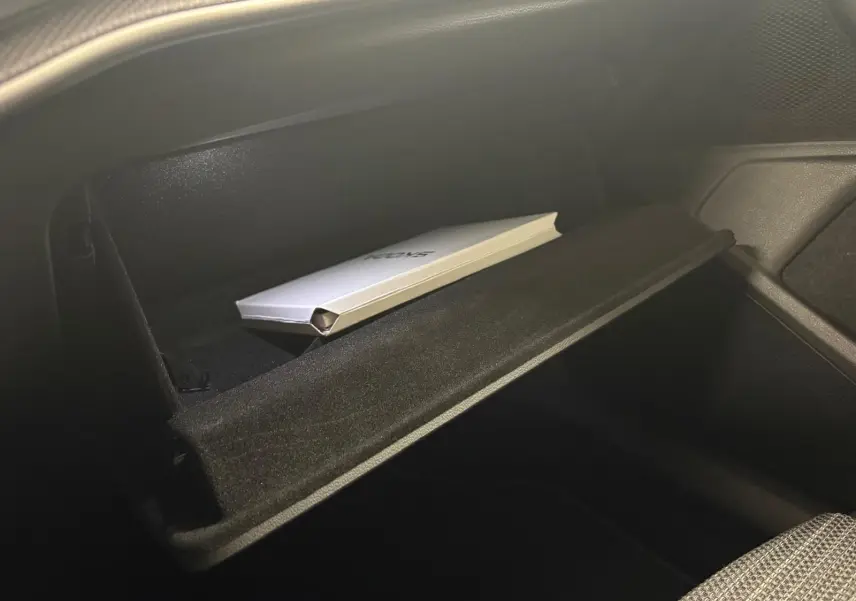 Gros plan sur la boîte à gants ouverte du Skoda Superb Combi gris argent 2025, avec un manuel à l'intérieur.