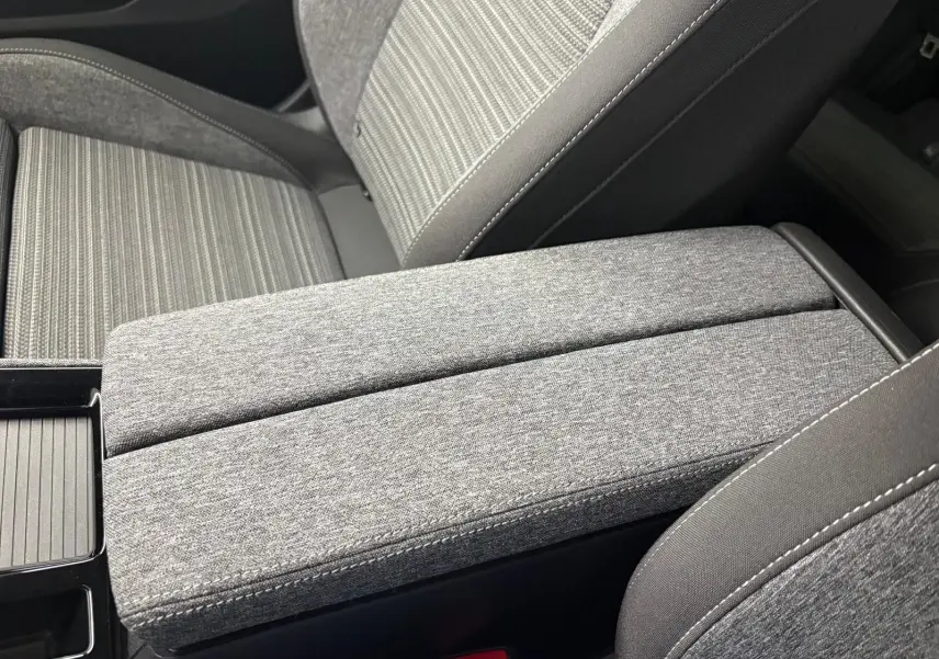 Détail de l'accoudoir central et siège avant en tissu gris à motifs, intérieur du Skoda Superb Combi 2025.