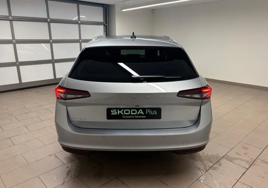 Vue arrière d'un Skoda Superb Combi gris argent 2025 dans un garage, avec feux arrière allumés et logo SKODA visible.