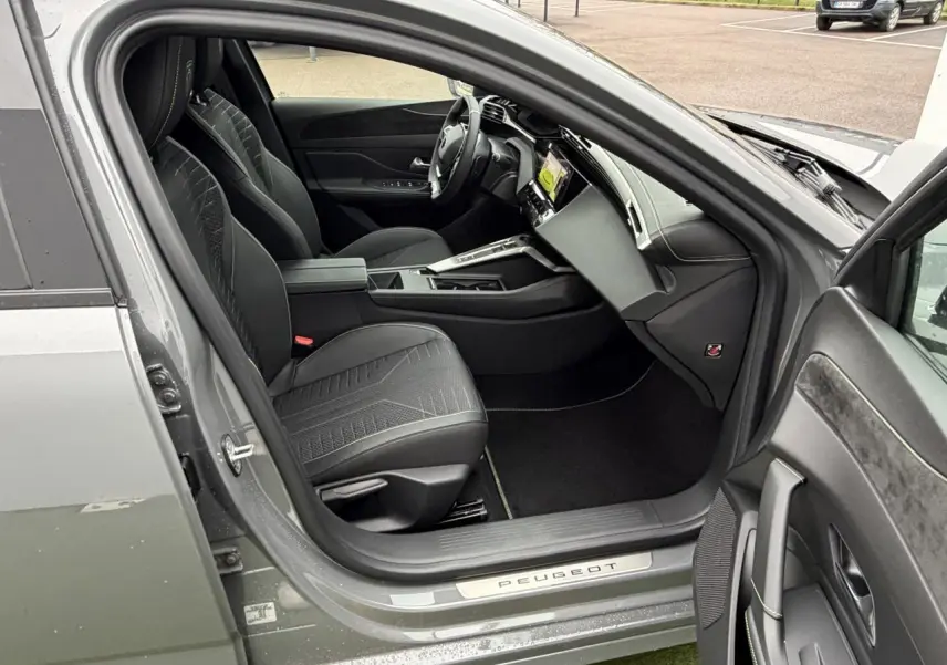 Vue intérieure côté conducteur de la Peugeot 308 gris selenium, montrant sièges noirs et tableau de bord moderne.