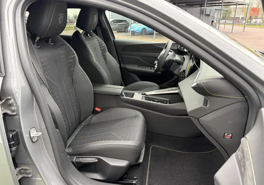 Vue intérieure côté conducteur du Peugeot 308 gris selenium, sièges noirs avec surpiqûres vert Adamite et volant compact cuir.