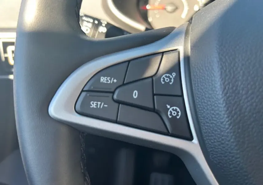 Gros plan sur les commandes de régulateur de vitesse à gauche du volant noir de la Dacia Sandero III Stepway 2025.