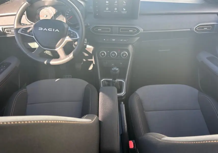 Vue intérieure avant de la Dacia Sandero III Stepway noire nacrée, volant, écran tactile et levier de vitesses manuel visibles.
