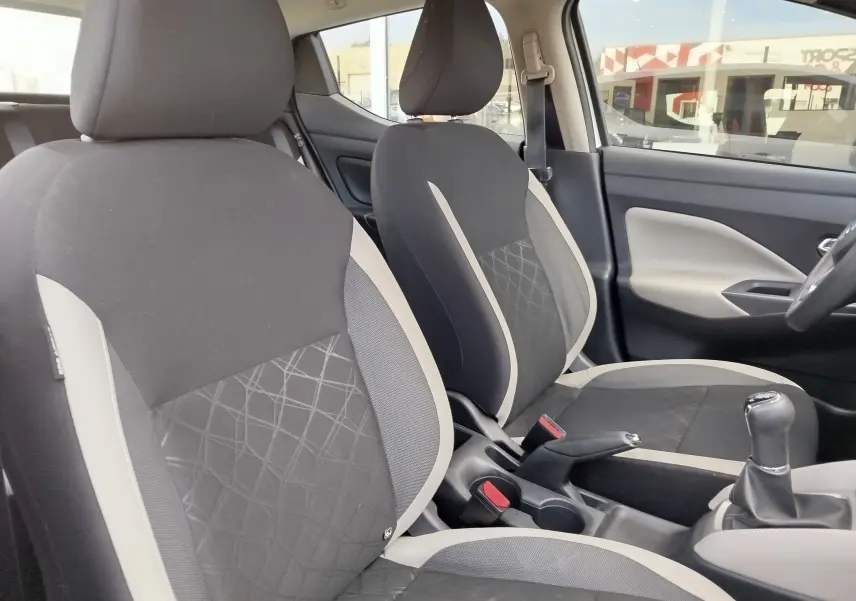 Vue intérieure côté conducteur de la Nissan Micra blanche 2019, sièges tissu gris et console avec levier de vitesse manuel.