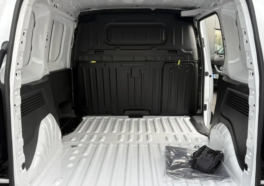 Vue intérieure de la zone de chargement blanche du Citroën Berlingo Van 2025 avec cloison noire et porte latérale ouverte.