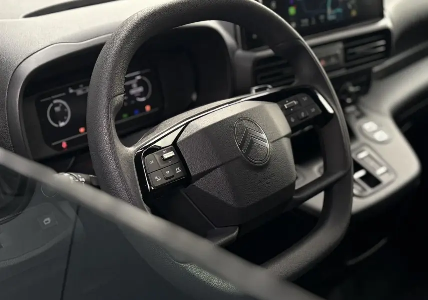 Vue rapprochée du volant multifonctions noir du Citroën Berlingo 2025 avec tableau de bord numérique en arrière-plan.