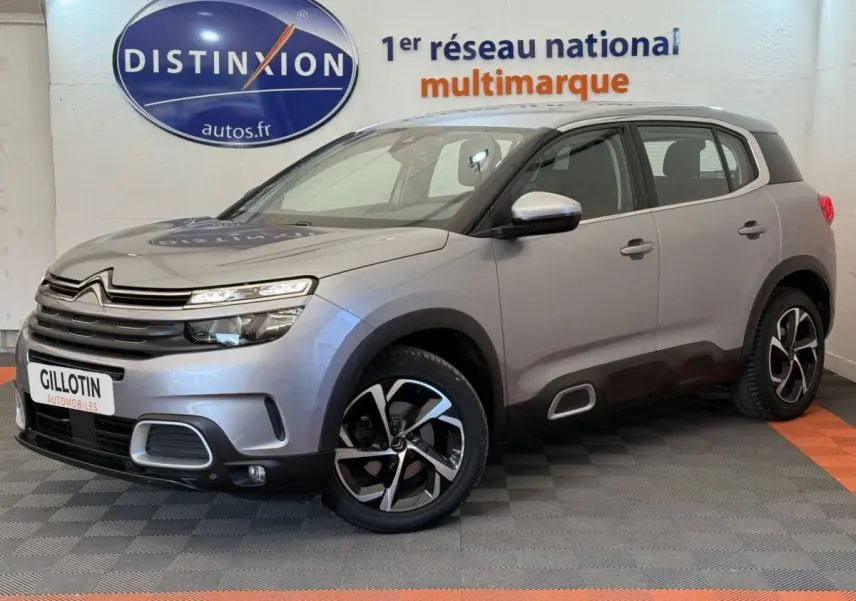 Citroën C5 Aircross gris clair en 3/4 avant droit, avec jantes noires et détails noirs sur les bas de caisse.