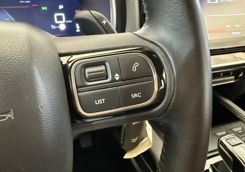 Gros plan sur les commandes gauche du volant cuir noir du Citroën C5 Aircross gris clair, avec écran tactile en arrière-plan.
