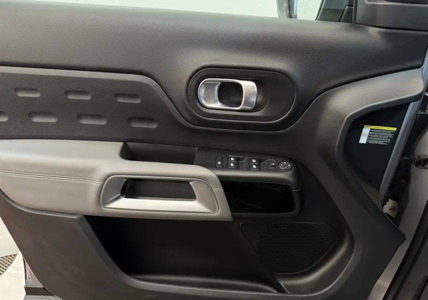 Gros plan sur la porte côté conducteur du Citroën C5 Aircross gris clair, montrant les commandes électriques et la poignée intérieure.
