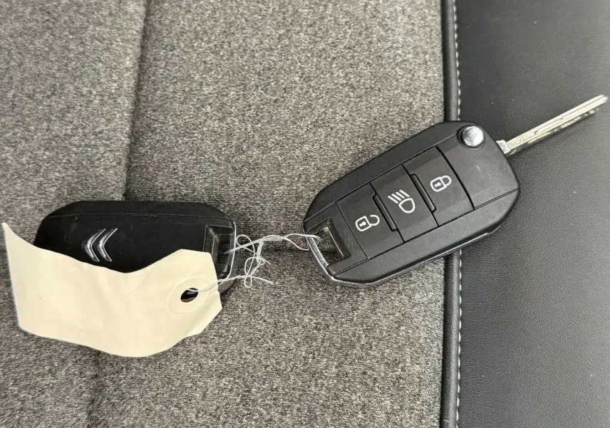 Clé de voiture CITROEN posée sur un siège gris, avec télécommande noire et étiquette attachée.